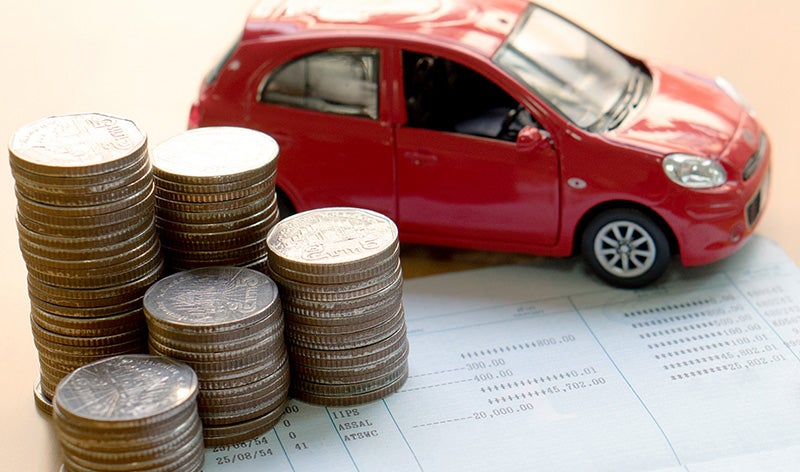 Stacks of coins placed beside a red model car on financial documents, representing vehicle financing, budgeting, or ownership costs